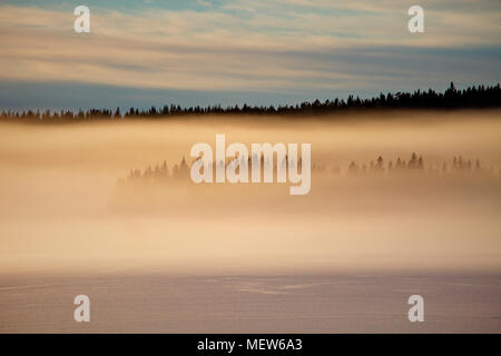 Vapors rising from a frozen lake are illuminated by the setting sun. Stock Photo