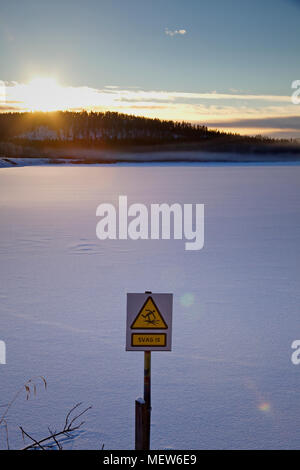 Frozen lake at dusk with a  sign warning in Swedish to walk on the thin ice. Stock Photo