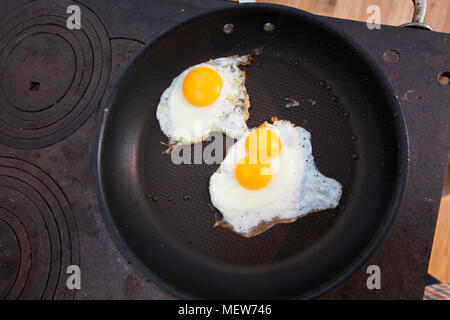 A double-yolked egg and a normal egg with one yolk are frying together in a non-sticking pan. Stock Photo
