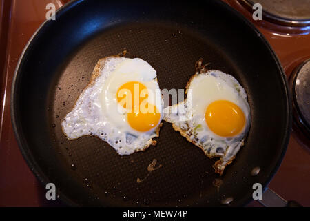 A double-yolked egg and a normal egg with one yolk are frying together in a non-sticking pan. Stock Photo