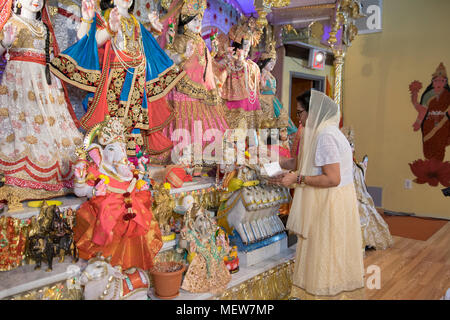 A woman places a flower on a statue on the altear at the Shri Lakshmi Narayan Mandir Hindu temple in Richmond Hill, Queens, New York. Stock Photo