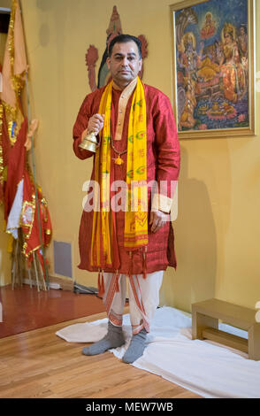 Portrait of a Hindu priest or pundit, ringing a bell during services at the Shri Lakshmi Narayan Mandir  temple in Richmond Hill, Queens, New York. Stock Photo