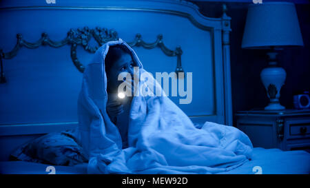 Girl scared of monsters covered in blanket with flashlight Stock Photo