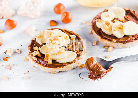 Crisp bread banana and chocolate snack. Healthy breakfast with hazel nuts. High key diet concept. Stock Photo