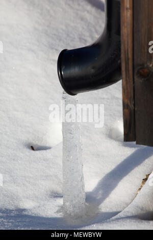 A stream of ice is emerging from a roof drain pipe on a cold winter day. Stock Photo