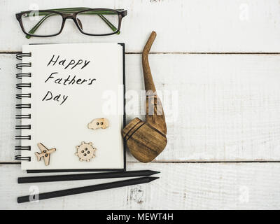 Smoking pipe and sketchbook with handwritten congratulation on Father's day on a beautiful, white table. Top view. Happy family concept Stock Photo