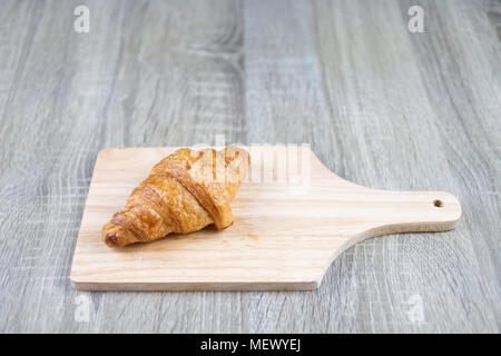 One piece of croissant is placed on a wooden cutting board and table on the gray wood with copy space Stock Photo