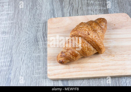 One piece of croissant is placed on a wooden cutting board and