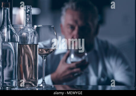 Close-up of wine bottles and glass with a sad man in the background Stock Photo