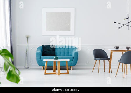 Turquoise couch with a dark pillow standing in light grey interior with molding on the wall and silver poster Stock Photo