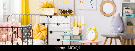 Yellow flowers and clock on table in cozy bedroom interior with grey chair and mockup Stock Photo