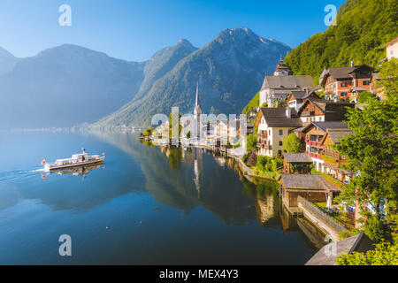 Classic postcard view of famous Hallstatt lakeside town with traditional ship in beautiful morning light at sunrise in summer, Salzkammergut, Austria Stock Photo