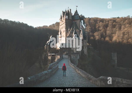 Panorama view of young explorer with backpack taking in the view at famous Eltz Castle at sunrise in fall, Rheinland-Pfalz, Germany