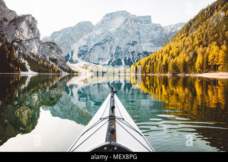 Beautiful view of kayak on a calm lake with amazing reflections of mountain peaks and trees with yellow autumn foliage in fall, Lago di Braies, Italy Stock Photo