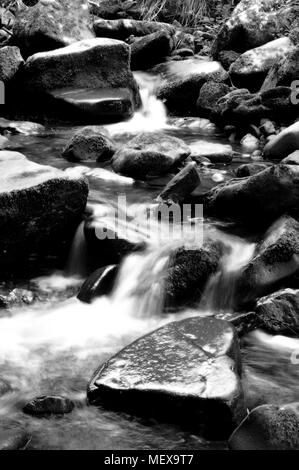 Misted water flowing through a Mountain rock riverbed in black and white Stock Photo