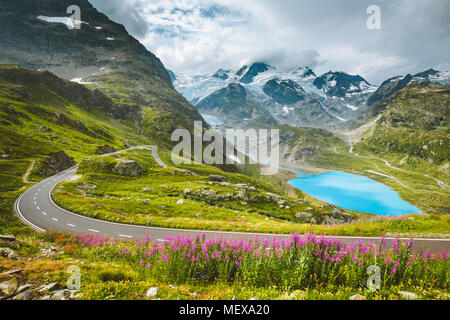 Beautiful view of winding mountain pass road in the Alps with mountain peaks, glaciers, lakes and green pastures with blooming flowers in summer Stock Photo