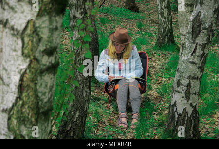 young caucasian female  artist sitting outdoors in a forest and drawing a picutre into her notebook Stock Photo