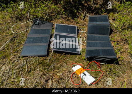 three portable solar panels recharging a batteries from a sun, outdoors on a hiking trail Stock Photo