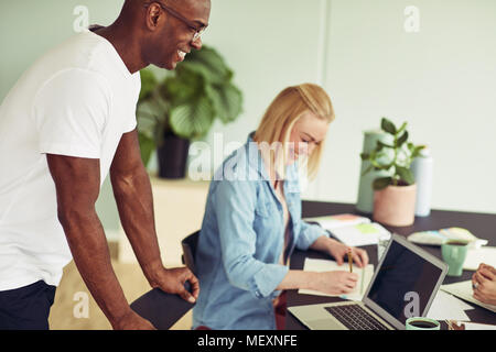 Two diverse business colleagues laughing while working together over a laptop at a table in an office Stock Photo
