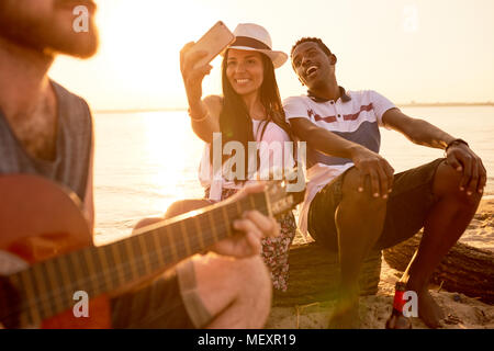 Excited multiethnic tourists photographing singer on beach Stock Photo