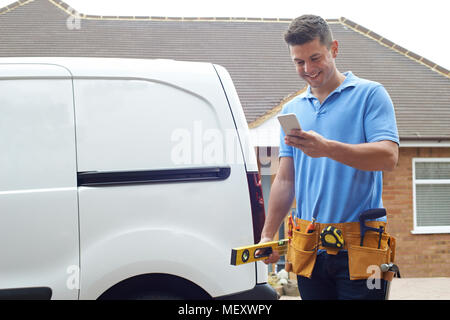 Builder With Van Checking Text Messages On Mobile Phone Outside House Stock Photo