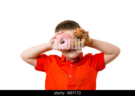 preschooler baby boy with two turquoise donuts on his eyes on white background wall. Child is having fun and looks through donut. Tasty food for kids. Funny time at home with sweet food. Stock Photo