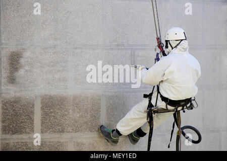 Rope access facade maintenance; A worker wearing a protective gear cleaning a stone exterior with sandblasting equipment Stock Photo