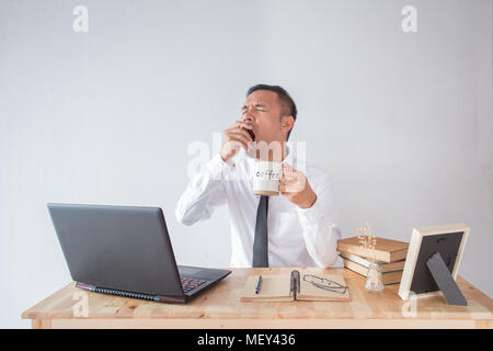 Young businessman yawning and drinking coffee to be energetic Stock Photo