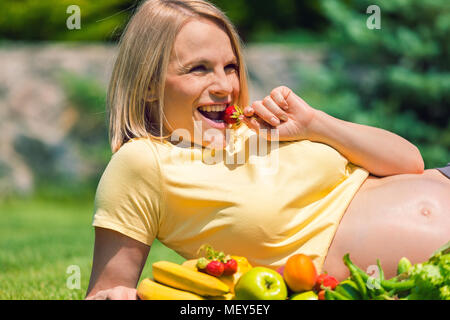 Pregnant woman lies on the grass and eats strawberries Stock Photo