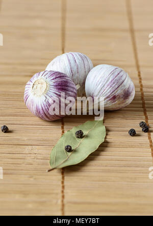 Three bulbs of garlic, bay leaf and black pepper on a mat, close up Stock Photo