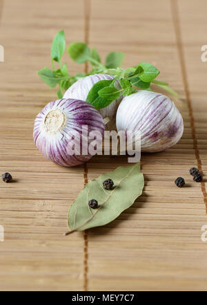 Three bulbs of garlic, bay leaf, black pepper and green basil on a mat Stock Photo