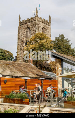 The tower of the 14thC medieval, Grade 1, Anglican, Holy Trinity Church at Skipton, North Yorkshire, UK. Restaurant patio in the foreground. Stock Photo