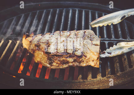 Beef steaks on the grill with flames. The chef flips a piece of meat beef on the grill with open fire. Stock Photo