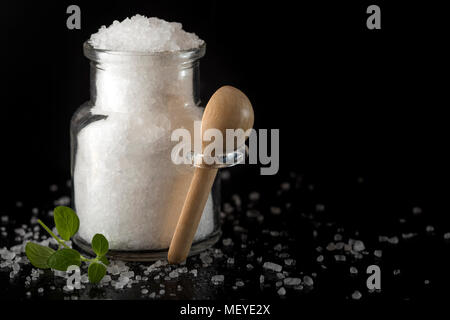 Glass jar filled with sea salt on dark slate background with green oregano Stock Photo