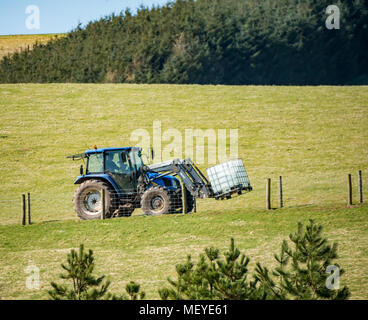 Farmer driving a Quicke tractor up a hill track delivering a plastic tank of water, Scottish Borders, Scotland, UK Stock Photo