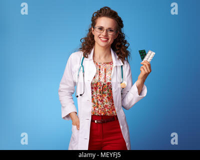happy paediatrist woman in white medical robe showing pills in a blister pack on blue background Stock Photo