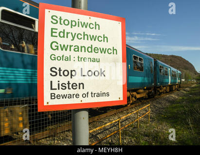 Warning sign on a footpath that crossing a railway line with a commuter train passing Stock Photo