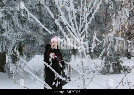 Beautiful smiling woman in fur coat and pink hat among the snow-covered trees Stock Photo