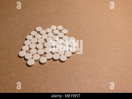 a pile of tablets isolated on a cardboard paper. A pile of beige medical tablets on a brown background Stock Photo