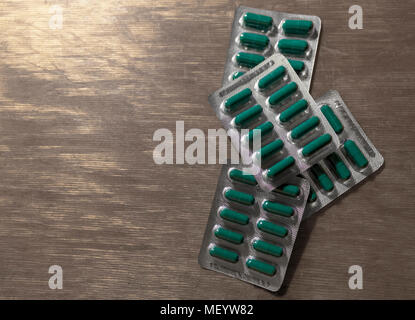 four blisters of green tablets lying one on top of the other on a wooden surface Stock Photo