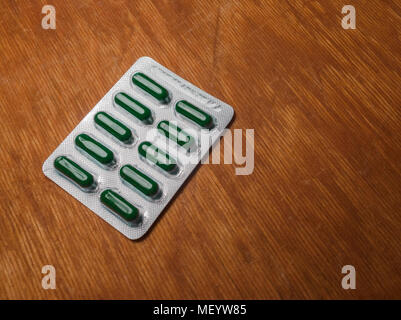 Green pills in blister pack on the old scratched wooden surface. Blister with green pills on a grungy wooden surface. Blister with copy space Stock Photo