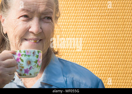 portrait of old grandmother outdoors at sun day. caucasian granny drinking hot coffee, tea in morning. elderly woman enjoying breakfast, holding warm mug, cup. positive senior lady smile Stock Photo