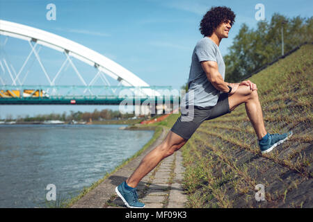 Male runner doing stretching exercise on walled coast, preparing for morning workout. Stock Photo