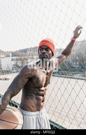 Portrait of muscular barechested basketball player standing at fence Stock Photo