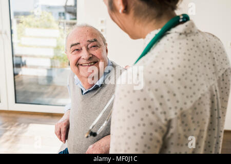 Senior man smiling at nurse at home Stock Photo