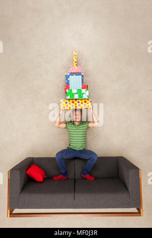 Man sitting on couch, balancing pile of presents on his head Stock Photo