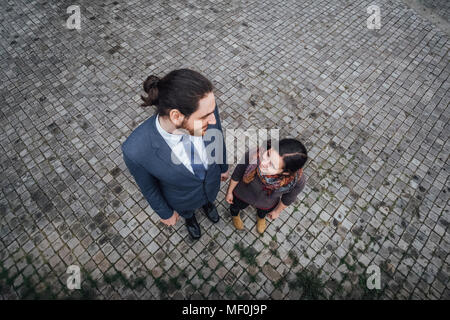 Woman and businessman standing on cobblestones smiling at each other Stock Photo