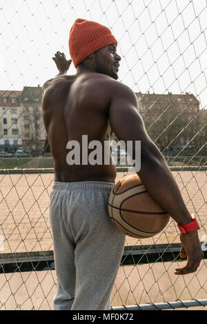 Rear view of muscular barechested basketball player standing at fence Stock Photo