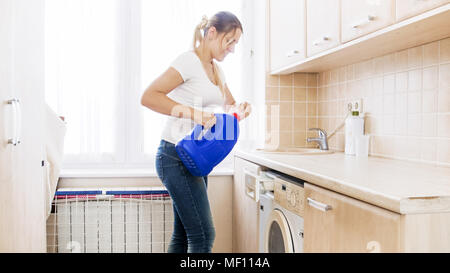Young blonde woman opens big bottle with washing detergent at laundry Stock Photo