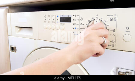 Closeup image of young woman setting water temperature on washing machine Stock Photo